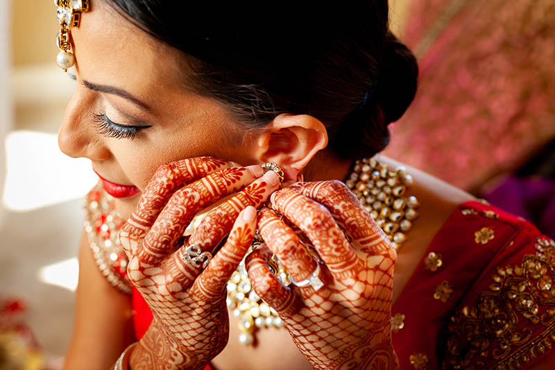 Indian bride with henna on hands, putting on earing